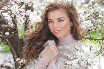 Young beautiful girl on spring flower background. Attractive woman closeup portrait. Lady with blond curly hair outdoor.