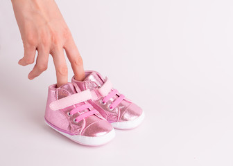 Children's sneakers on a white background. Small children's shoes worn on the fingers of a female hand. The concept of the first children's steps.