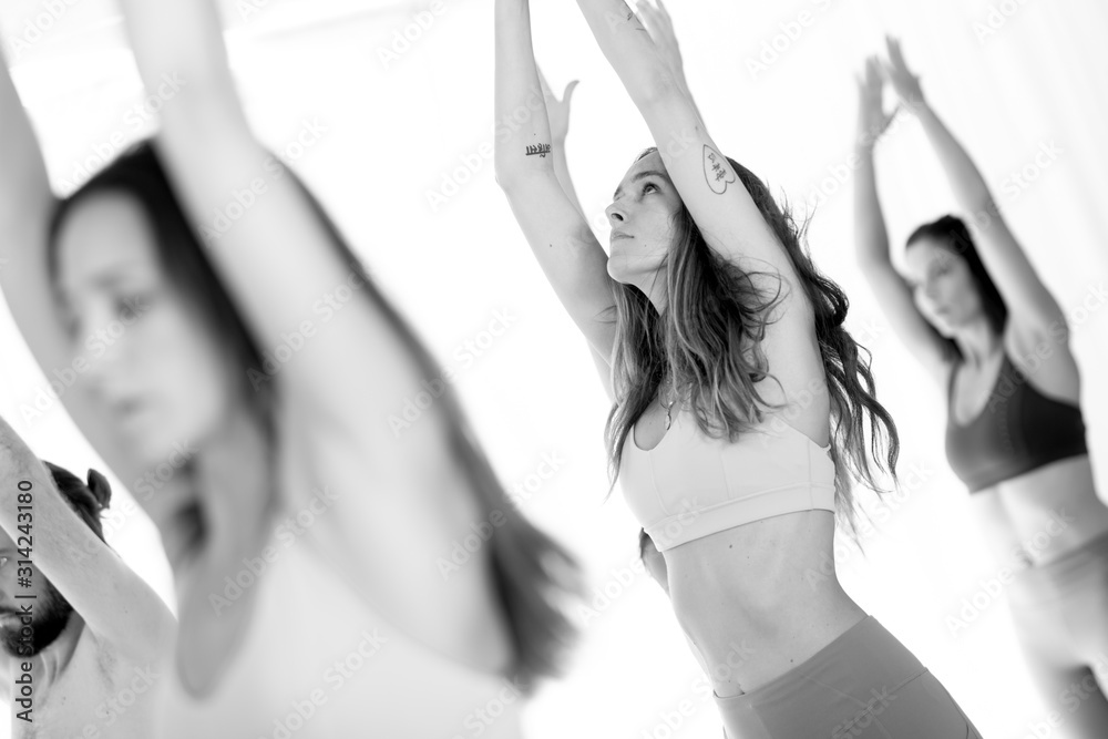 Group of young sporty attractive women in yoga studio, practicing yoga lesson with instructor, standing, stretching and relaxing after workout . Healthy active lifestyle, working out. Black and white. - obrazy, fototapety, plakaty 