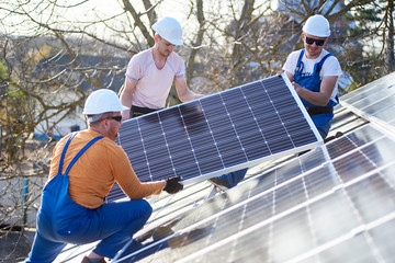 Wall Mural - Male engineers installing stand-alone solar photovoltaic panel system. Electricians mounting blue solar module on roof of modern house. Alternative energy ecological concept.