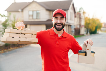 Sticker - Image of joyful young delivery man holding pizza boxes and coffee