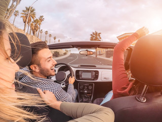 Happy friends having fun on convertible car during road trip - Group trendy young people enjoying vacation together in tropical city - Youth culture lifestyle and travel transportation concept