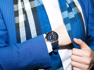 Wall Mural - Closeup fashion image of luxury watch on wrist of man.body detail of a business man.Man's hand in blue pants pocket closeup at white background.Man wearing blue jacket and white shirt.Not isolated