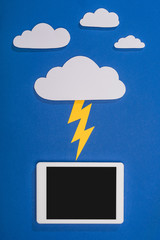 Wall Mural - top view of white paper cut clouds with lighting hitting digital tablet on blue background