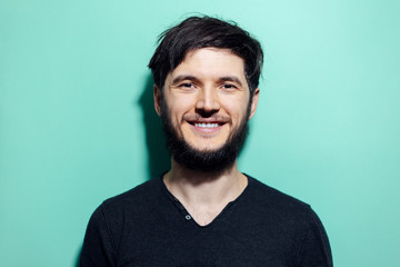 Canvas Print - Studio portrait of young smiling bearded man with disheveled hair on background of aqua menthe color.