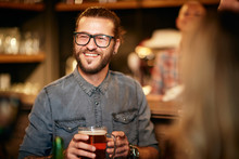 Handsome Caucasian Hipster Standing At Pub With Friends, Holding Pint Of Beer And Enjoying Night Out.