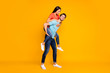 © deagreez - Full body photo of two funny people guy carrying lady piggyback meet summer adventures together wear casual trendy blue orange t-shirts jeans isolated yellow color background
