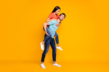 Full body photo of two funny people guy carrying lady piggyback meet summer adventures together wear casual trendy blue orange t-shirts jeans isolated yellow color background