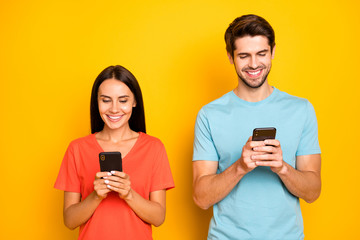 Photo of two funny guy lady people couple hold telephones arms interested reading social network article wear casual blue orange t-shirts isolated yellow color background
