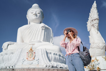 Traveling by Thailand. Pretty young woman taking photo in the Big Buddha Temple, famous Phuket sightseeing.