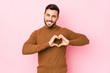 © Asier - Young caucasian man against a pink background isolated smiling and showing a heart shape with hands.