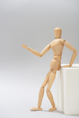 Wall Mural - Wooden dummy by white stand pointing with hand on grey background