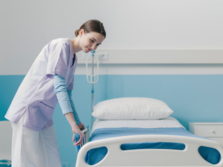 Young trainee nurse working at the hospital and adjusting bed rails