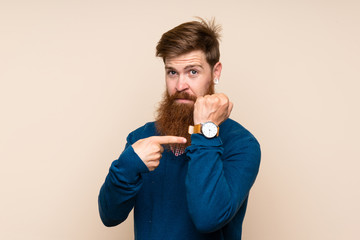 Redhead man with long beard over isolated background showing the hand watch with serious expression