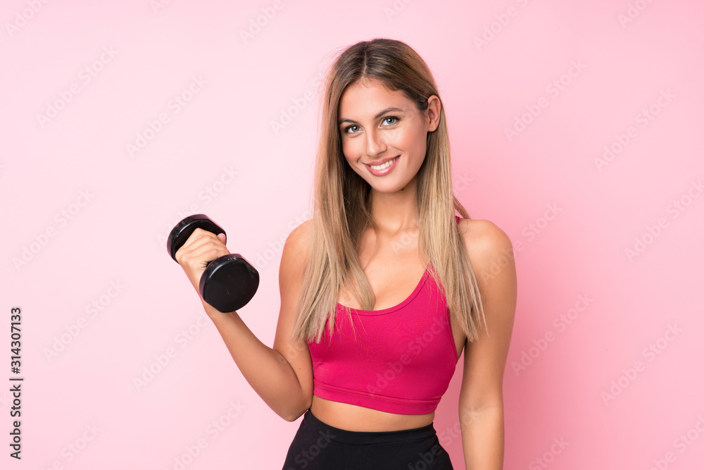 Young sport blonde woman over isolated pink background making weightlifting with kettlebell - obrazy, fototapety, plakaty 