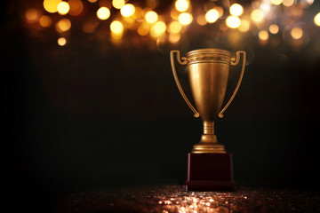 Wall Mural - low key image of trophy over wooden table and dark background, with abstract shiny lights