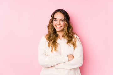 Young curvy woman posing in a pink background isolated who feels confident, crossing arms with determination.