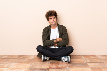 Wall Mural - Young caucasian man sitting on the floor with confuse face expression