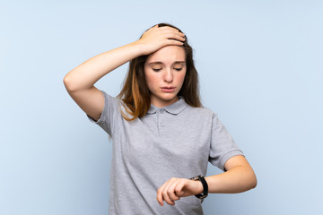 Wall Mural - Young brunette girl over isolated blue background with wrist watch and surprised