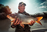 Happy young fisherman holds the big Carp fish (Cyprinus carpio) and smiles