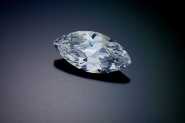 A faceted marquise cut diamond sits on a black reflective background.