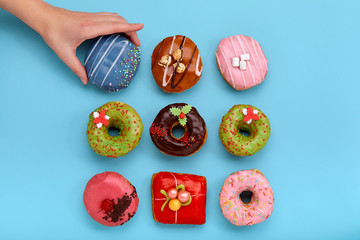 Wall Mural - Various colorful donuts on blue background, female hand takes a donut. Top view.