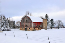 Snowy Winter Rural Landscape With Red Barn.Scenic View With Old Style Red Barn Between Trees Against Cloudy Sky After Heavy Snowfall.Wisconsin, Midwest USA Rural Life At Winter And Farming Background.
