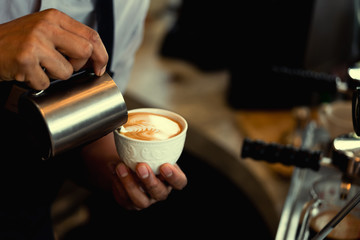 Wall Mural - Close-up of male barista hand holding and pouring hot milk for prepare latte art on a green cup of cappuccino coffee. vintage color tone.