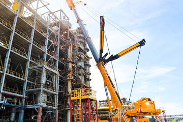 Construction and installation work with a powerful construction crane of a large new industrial oil refining petrochemical chemical plant with pipes, columns, railings, stairs and equipment