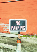 A No Parking Sign On An Orange Cone In A Parking Lot In Front Of A Red Wall.