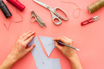 Tailor working. Women hands drawing patterns for clothes on pink background top-down