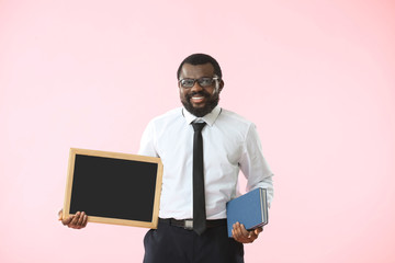 Wall Mural - African-American teacher with chalkboard and books on color background