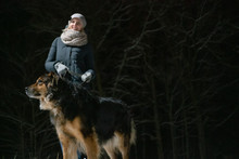 Girl With A German Shepherd Walking On A Winter Night In The Park. Photo On The Background Of A Dark Forest.