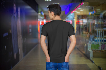 Wall Mural - Template of a black T-shirt on a young guy, on the background in the store, back view.