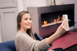 Young woman uses smartphone for video chat in front of fireplace