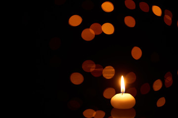 Wall Mural - burning candle glowing in dark with bokeh lights on background