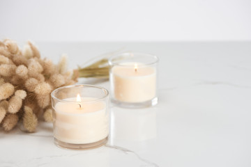 Sticker - selective focus of fluffy bunny tail grass and burning white candles in glass glowing on marble white surface