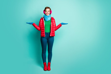 Wall Mural - Full body photo of pretty lady hold two arms proposing novelty products wear casual red overcoat blue scarf pink ear covers jumper pants shoes isolated teal color background