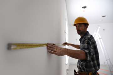 Canvas Print - Worker measuring white wall indoors, focus on hand