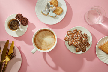 Wall Mural - Top view of cups of coffee with fresh cookies and water on pink background