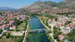 Aerial view of Arslanagic`s bridge on Trebisnjica river in Trebinje Old Town. Bosnia and Herzegovina. Summer sunny day, Turquoise water, mountains, trees, blue sky, small houses.