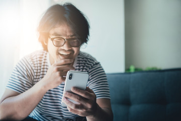 Wall Mural - using cell phone.portrait young asian man wear eye glasses Smiling cheerful look screen texting chatting on mobile.contact connecting people freedom life style concept