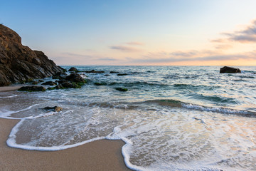 sunrise on the beach. beautiful summer scenery. rocks on the sand. calm waves on the water. clouds on the sky. wide panoramic view