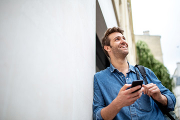 older man leaning against wall with cellphone and looking away