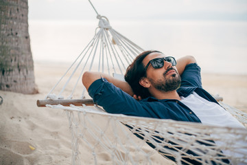 Wall Mural - A man enjoys calm, lies in a hammock on the background of the ocean and sunset.