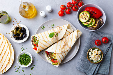 Wrap sandwich with grilled vegetables and feta cheese on a plate. Grey background. Top view.