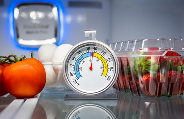 Refrigerator thermometer with colorful food in cold storage unit. Refrigeration safety gauge displaying safe food temperature.