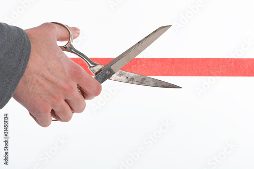 Fotomural Male hand cutting through red tape with scissors isolated on white with a shallo