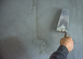 Worker hand plastering and smoothing concrete wall with cement and a steel trowel, on construction site