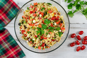 Closeup of pasta salad with fresh vegetables and herbs on a white wood background